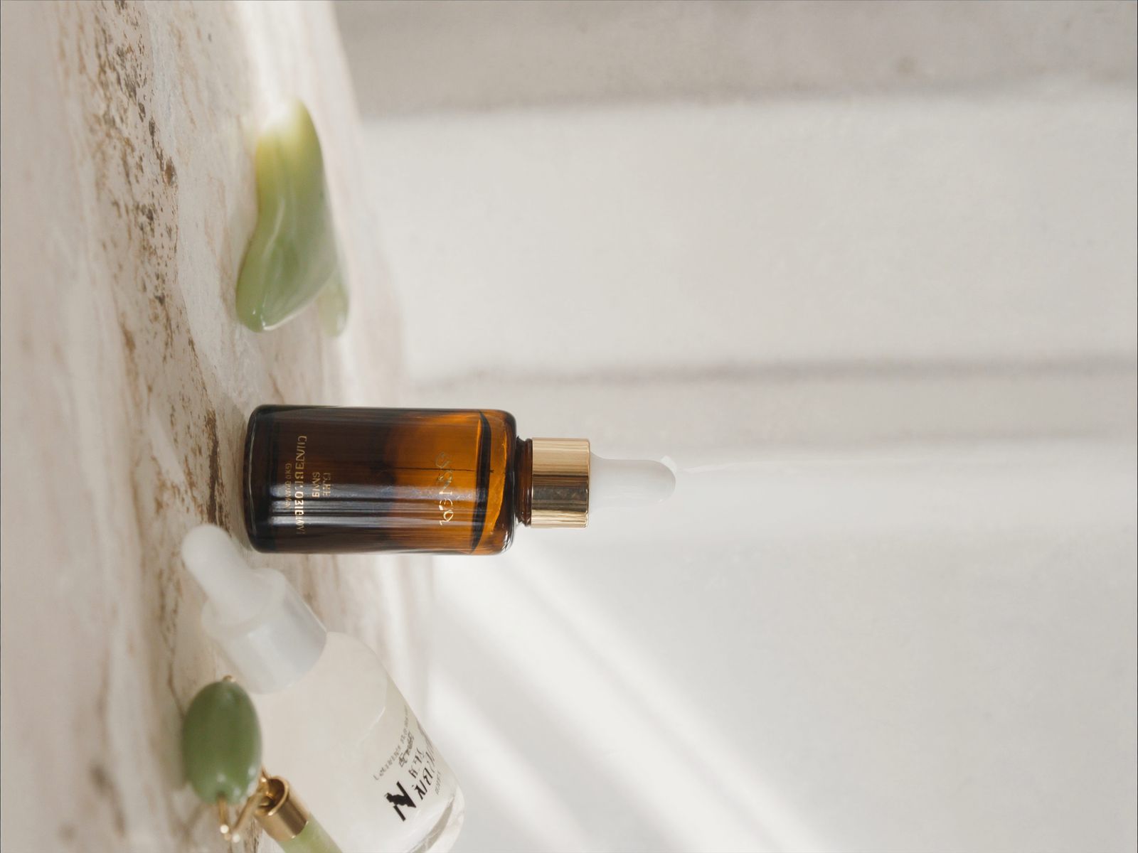 Skincare serum bottles and a jade roller on stone