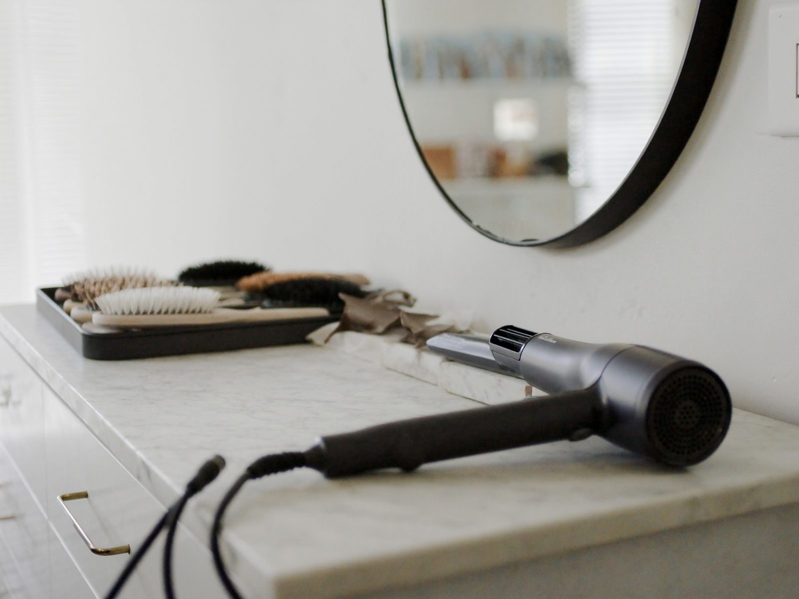 A blow dryer, round brushes and a flat iron at a styling station