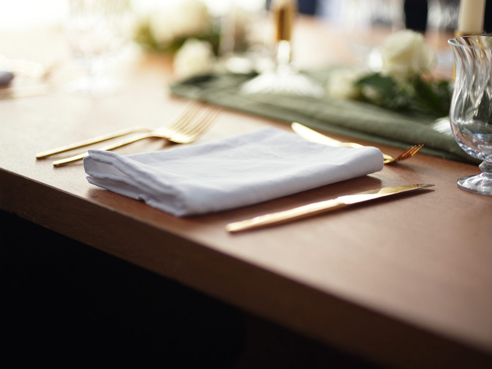 A table setting with linen, gold cutlery and white roses